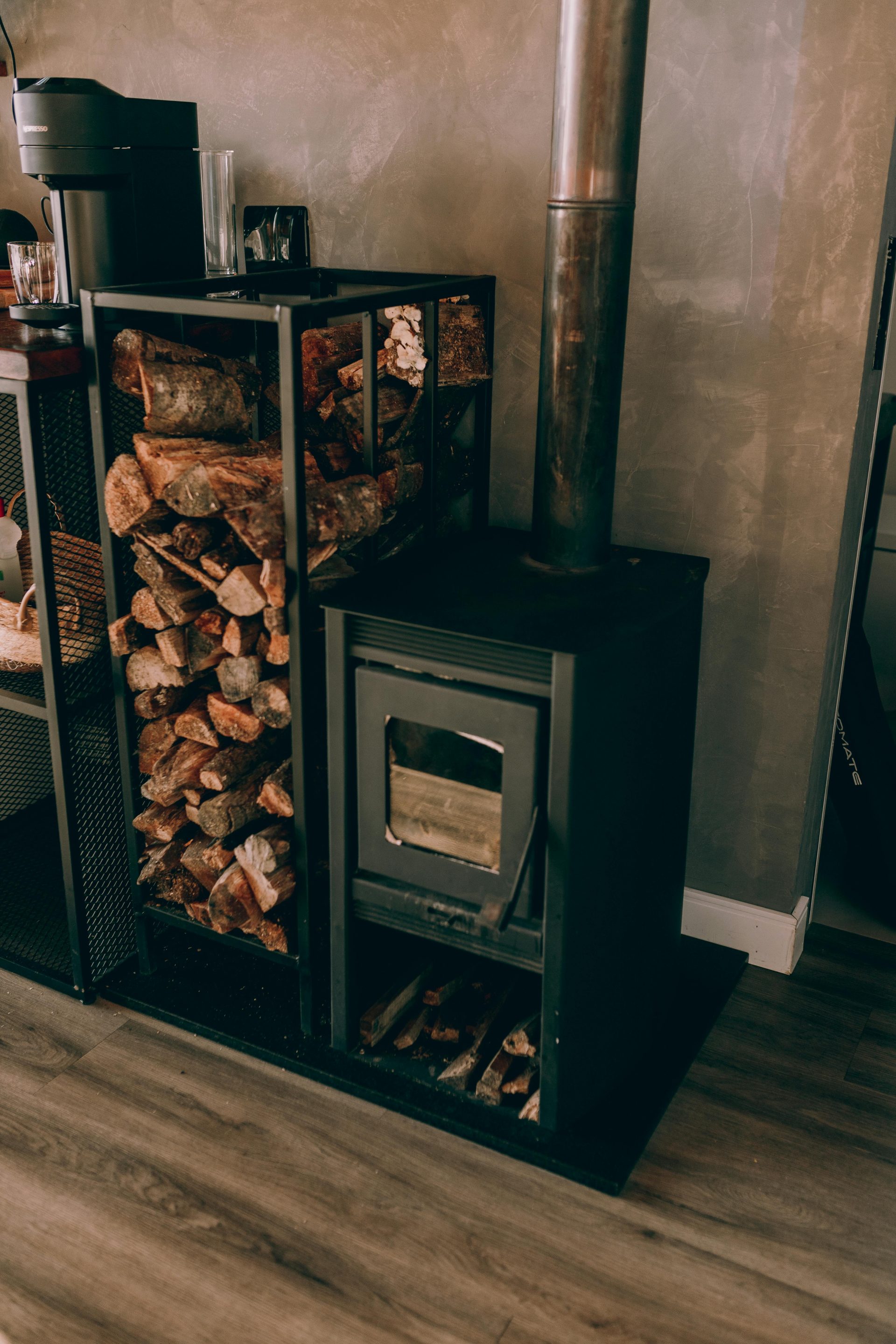 Eine stilvolle Innenraumszene mit einem modernen Holzofen und gestapeltem Brennholz, die eine warme und einladende Atmosphäre schafft.
